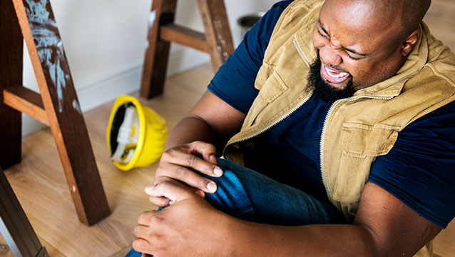 A man sits on the floor in a room under construction holding his knee in pain. Harder, Wells, Baron and Manning workers' compensation lawyers in Oregon help after job injuries.